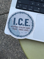 A sticker with the text "ICE" and "KEEPING STOLEN LAND 'PURE' SINCE 2003" is placed on a laptop keyboard.