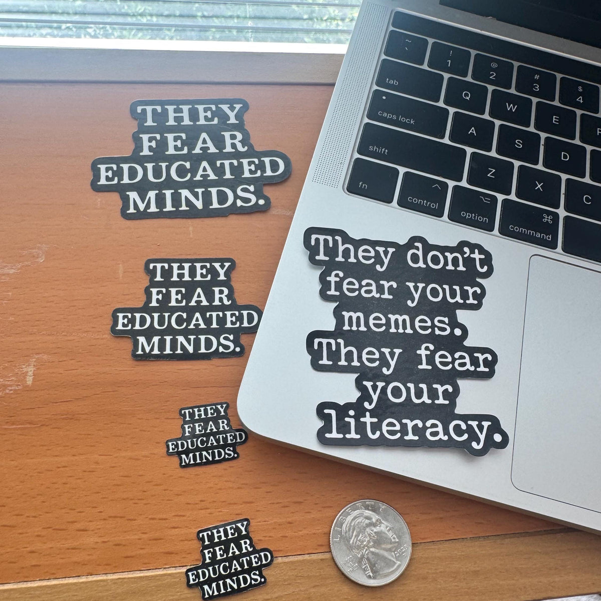Stickers on a laptop and desk with text about fear of educated minds and literacy.