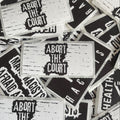 a collection of black and white stickers with the text "Abort the Court" printed on them.