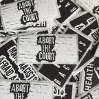 a collection of black and white stickers with the text "Abort the Court" printed on them.