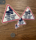 Three funny meme stickers of varying sizes showing the I.C.E. boot stomping a feather, shown with a ruler and a quarter for scale on a wood table.