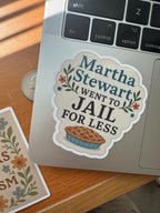 A funny sticker 'Martha Stewart Went To Jail For Less' featuring a pie illustration and floral accents, stuck on a laptop next to a quarter for scale.