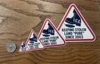 Four political satire stickers in graduated sizes from small to large, each depicting the I.C.E. boot crushing a feather, displayed beside a quarter on a wood table.