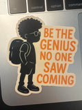 Black boy silhouette student motivation quote sticker with afro, glasses, and backpack beside bold orange text reading 'Be The Genius No One Saw Coming,' applied near a laptop keyboard.